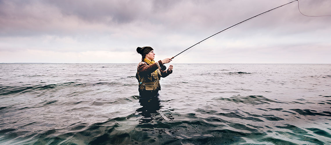 Bild på en man höftdjupt i vatten med fiskespö.