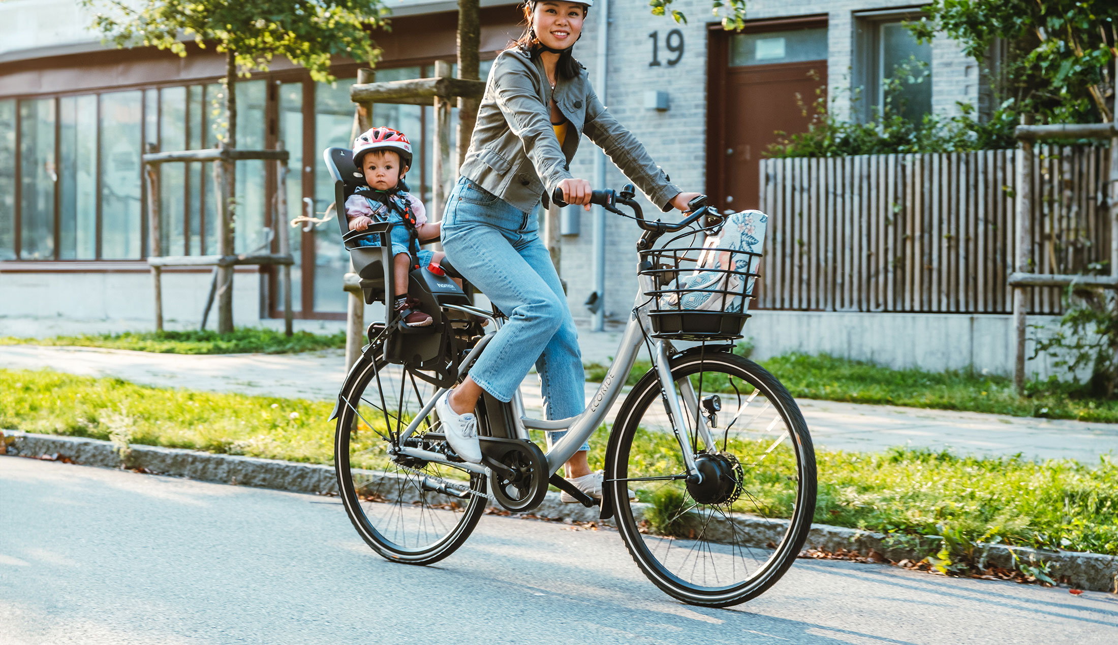 Kvinna cyklar på en Ecoride-cykel med ett barn i en stol på pakethållaren