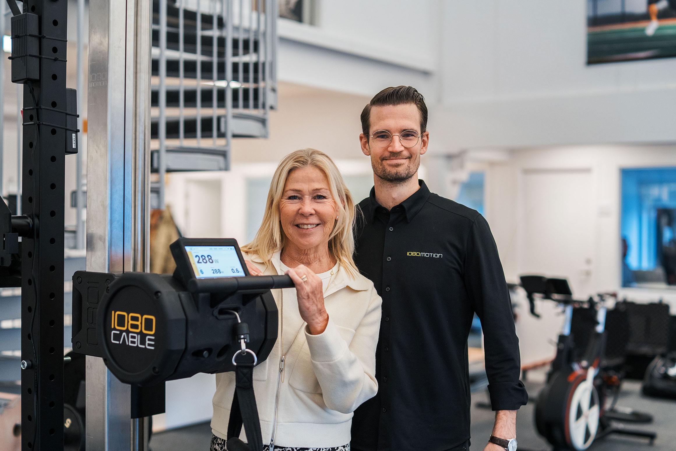 Anna-Carin Månsson och Per Nohlert står i ett gym och demonstrerar en av 1080Motions produkter.