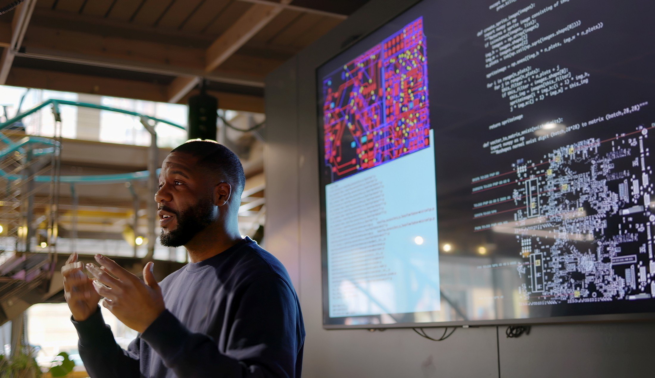 En man pratar till en publik utanför bild. Bakom honom syns kod på en skärm.