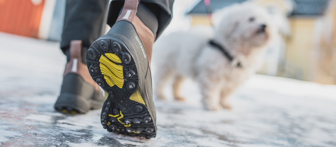 Bild på sulan på vinterkängor bakifrån. I bakgrunden en liten hund.