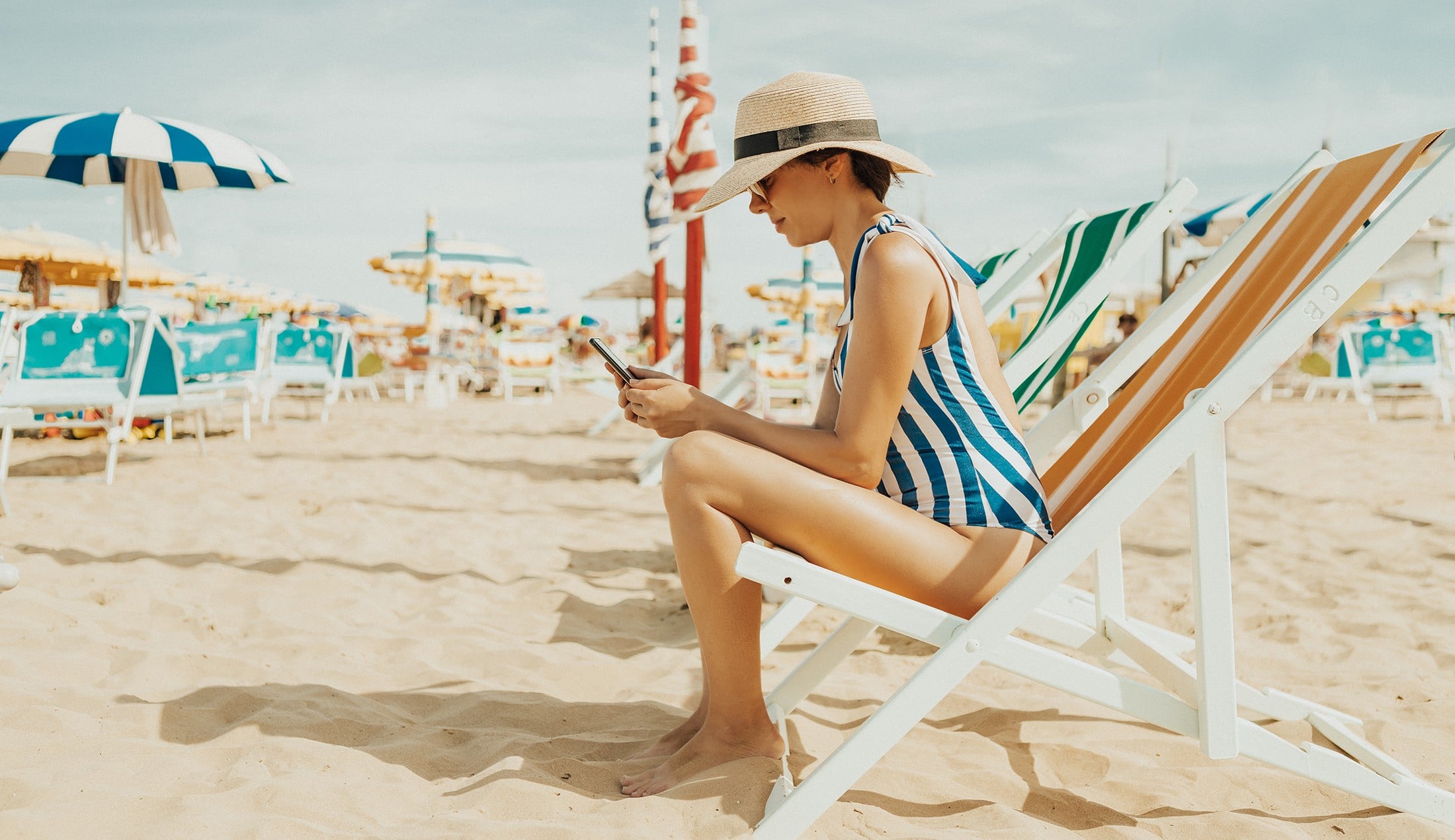 Woman sitting in a sun chair on a beach, reading on her mobile phone.