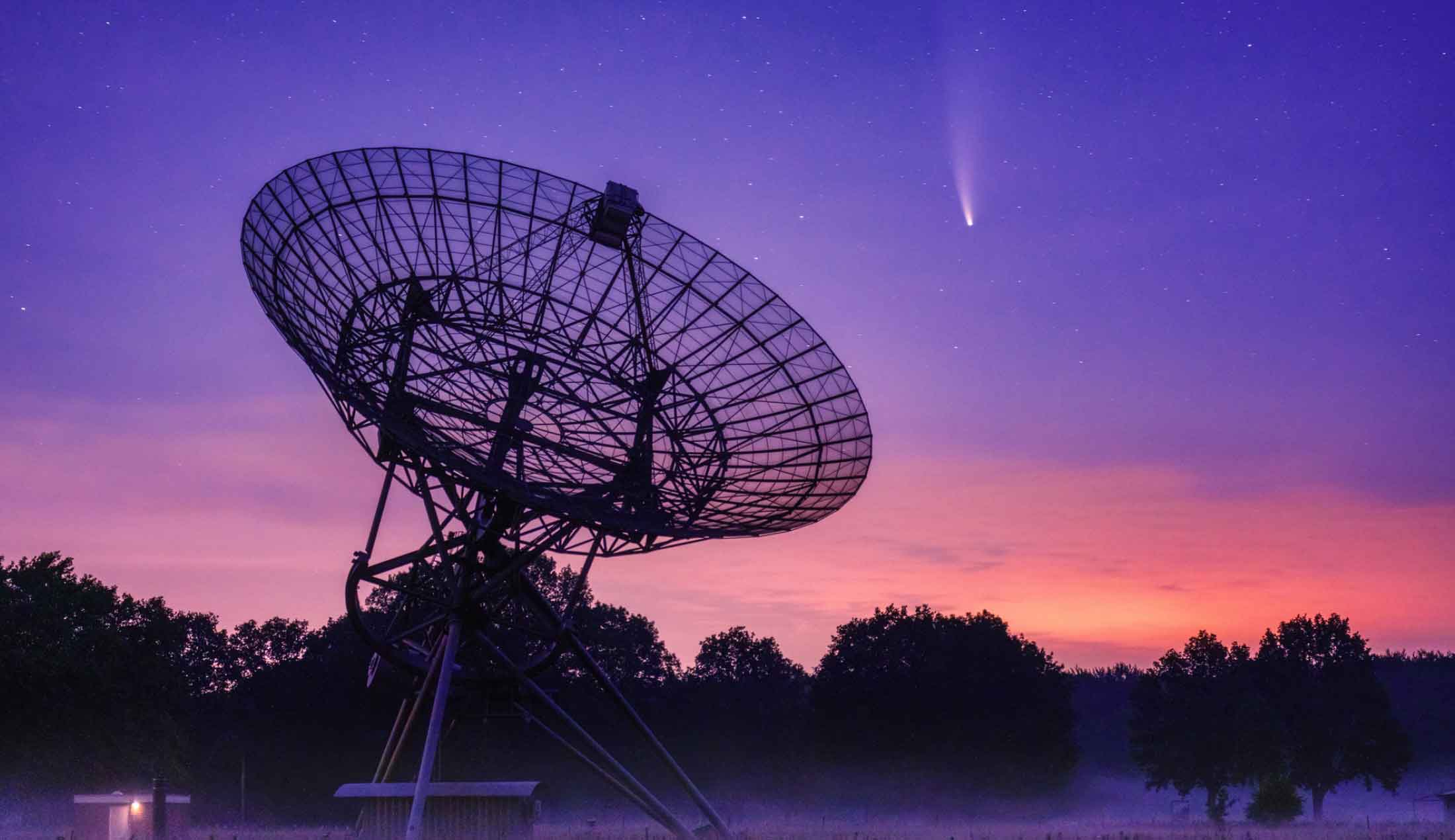 En stor parabolantenn riktad mot himlen. Bilden är tagen under nattetid.