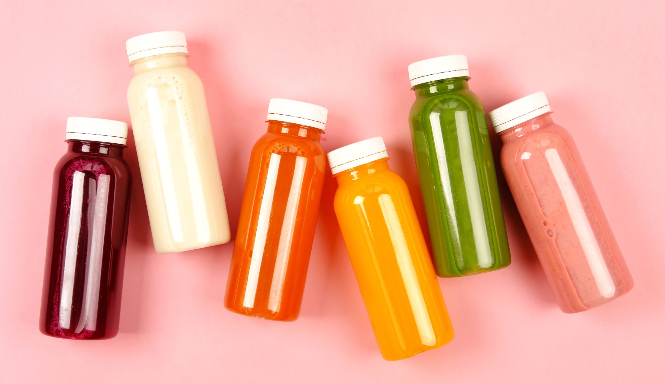 Fem plastflaskor fyllda med smoothie mot en enfärgad bakgrund.
