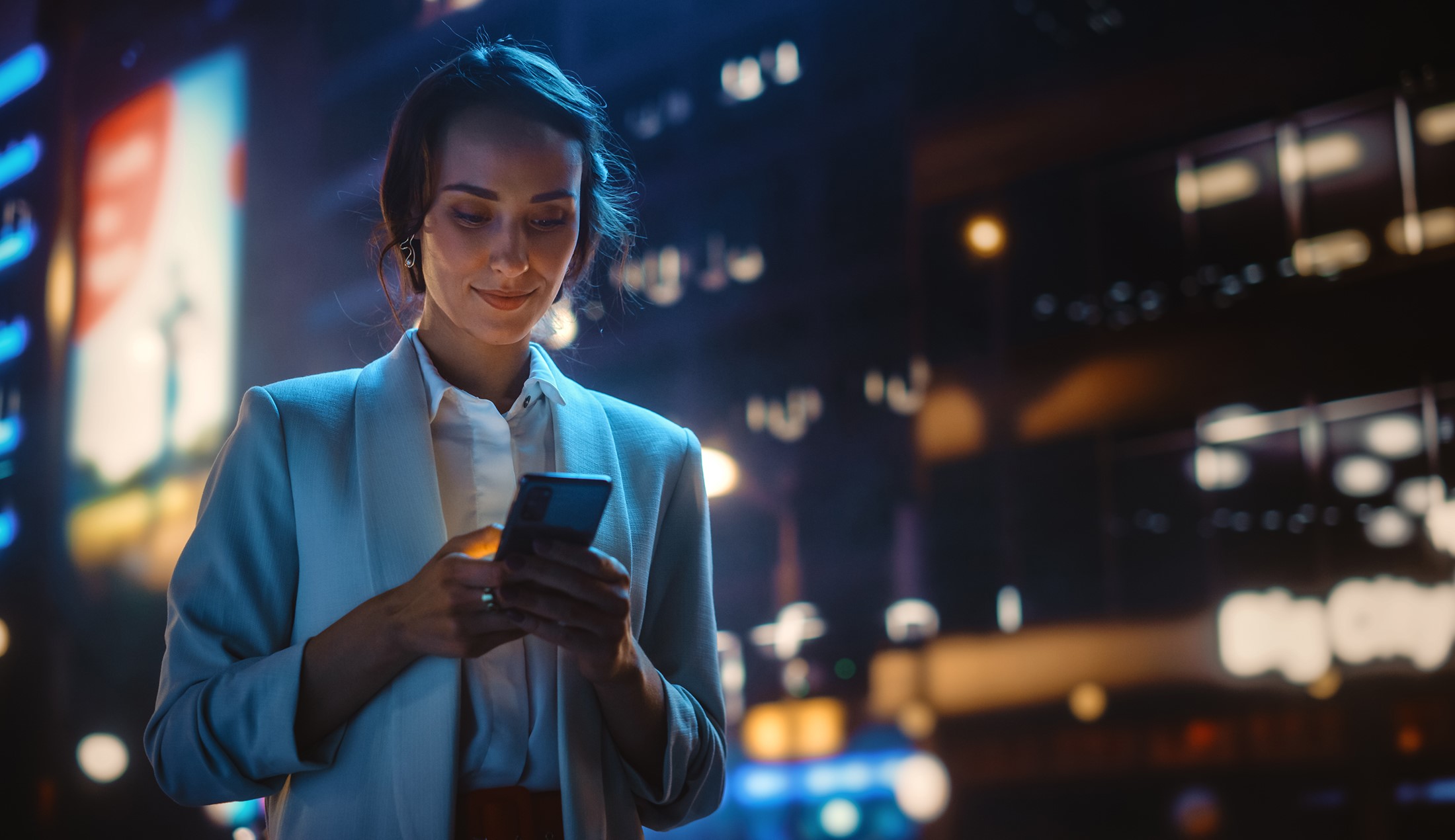 Kvinna tittar i sin mobil i en stad kvällstid