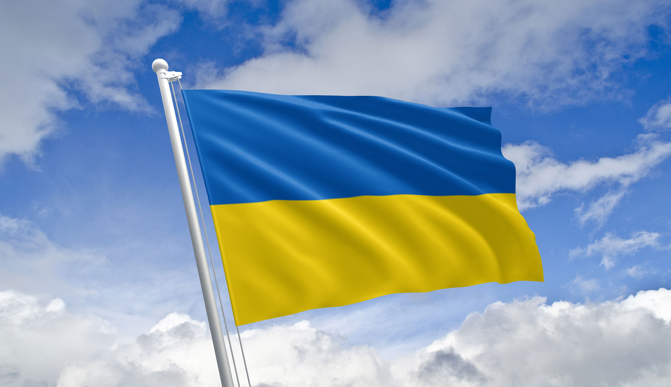 Ukrainas flagga vajar mot en blå himmel med vita moln.