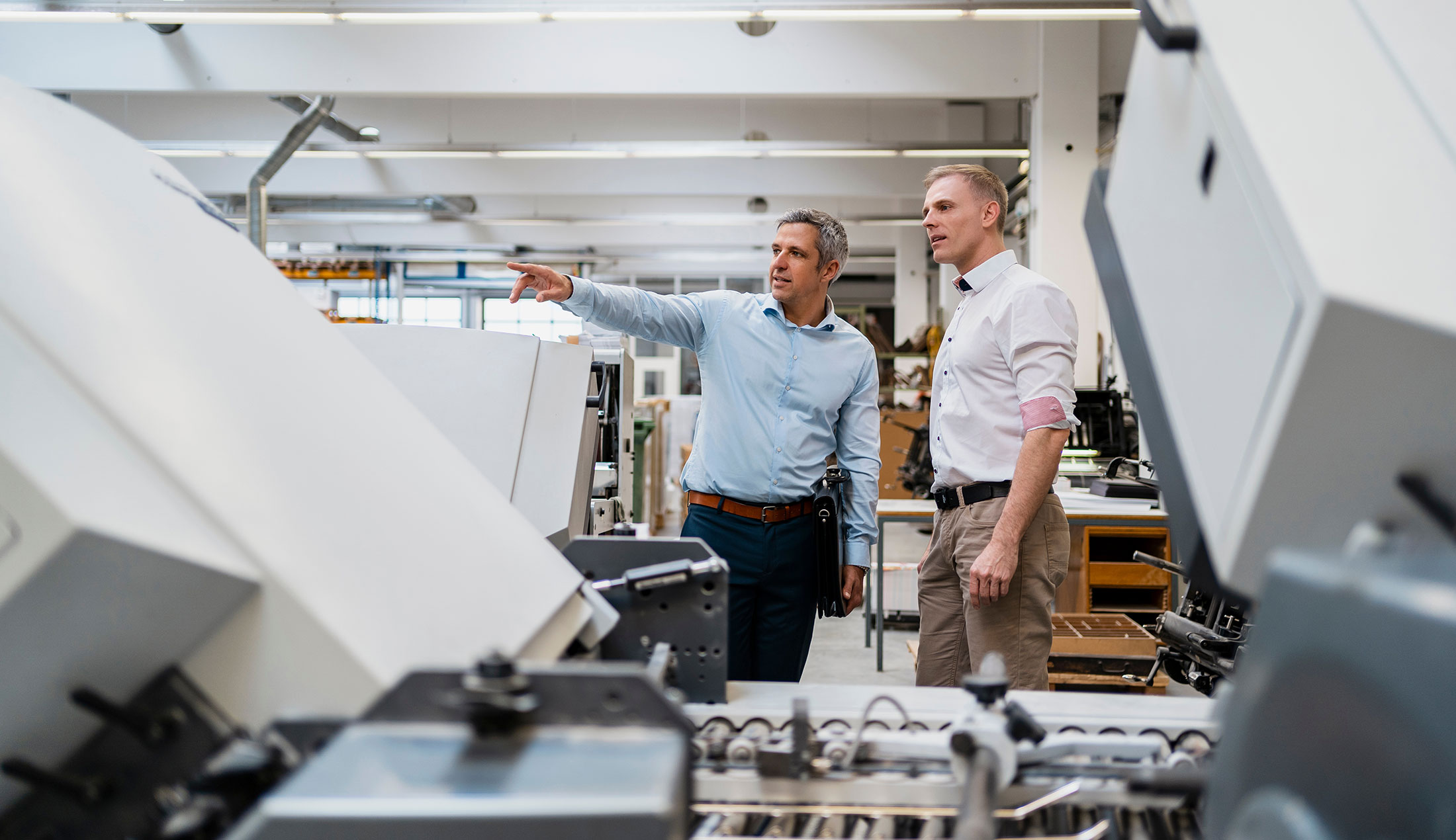 Two men standing surrounded by machinery in an industrial setting.
