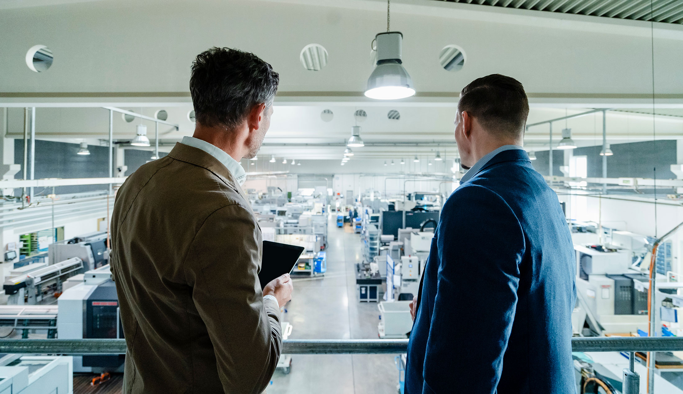 The backs of two men standing on an elevated section of the premises, looking down at the factory floor.