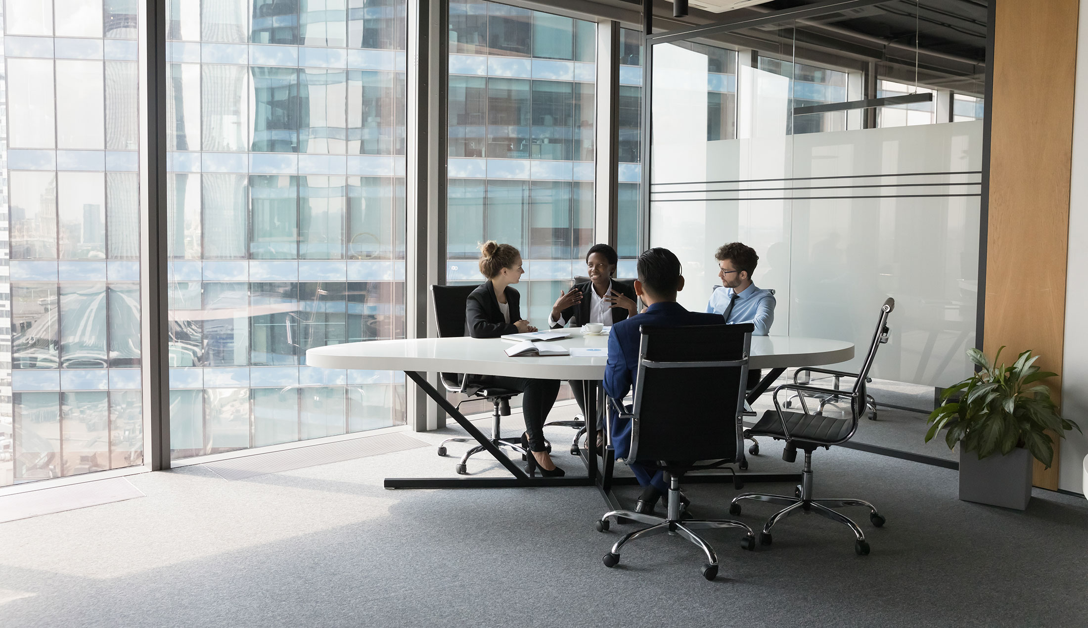 Four people gathered around a table in a conference room with floor-to-ceiling glass windows.