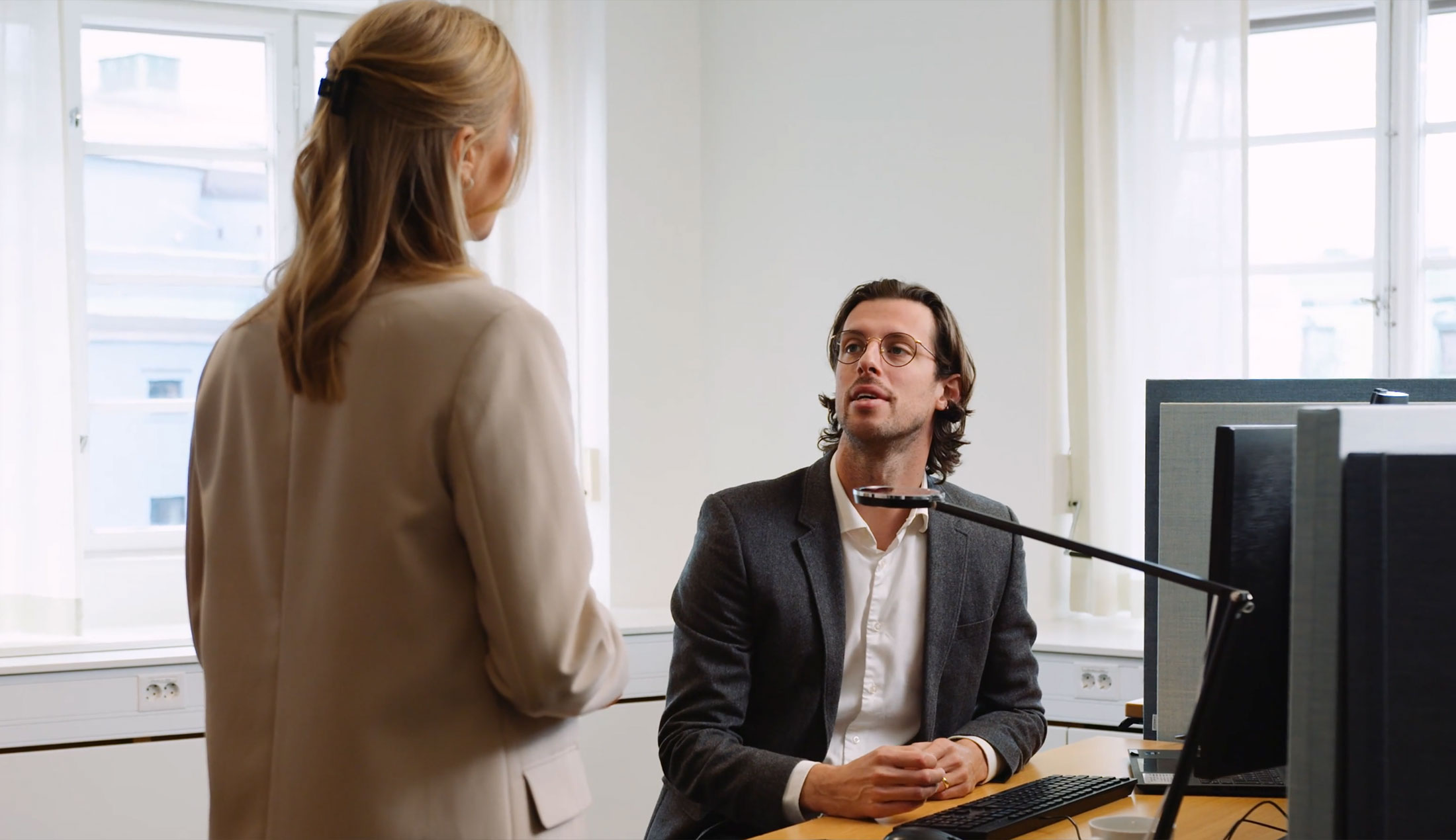 Juristen Alexander sitter vid ett skrivbord och pratar med en kollega som står bredvid