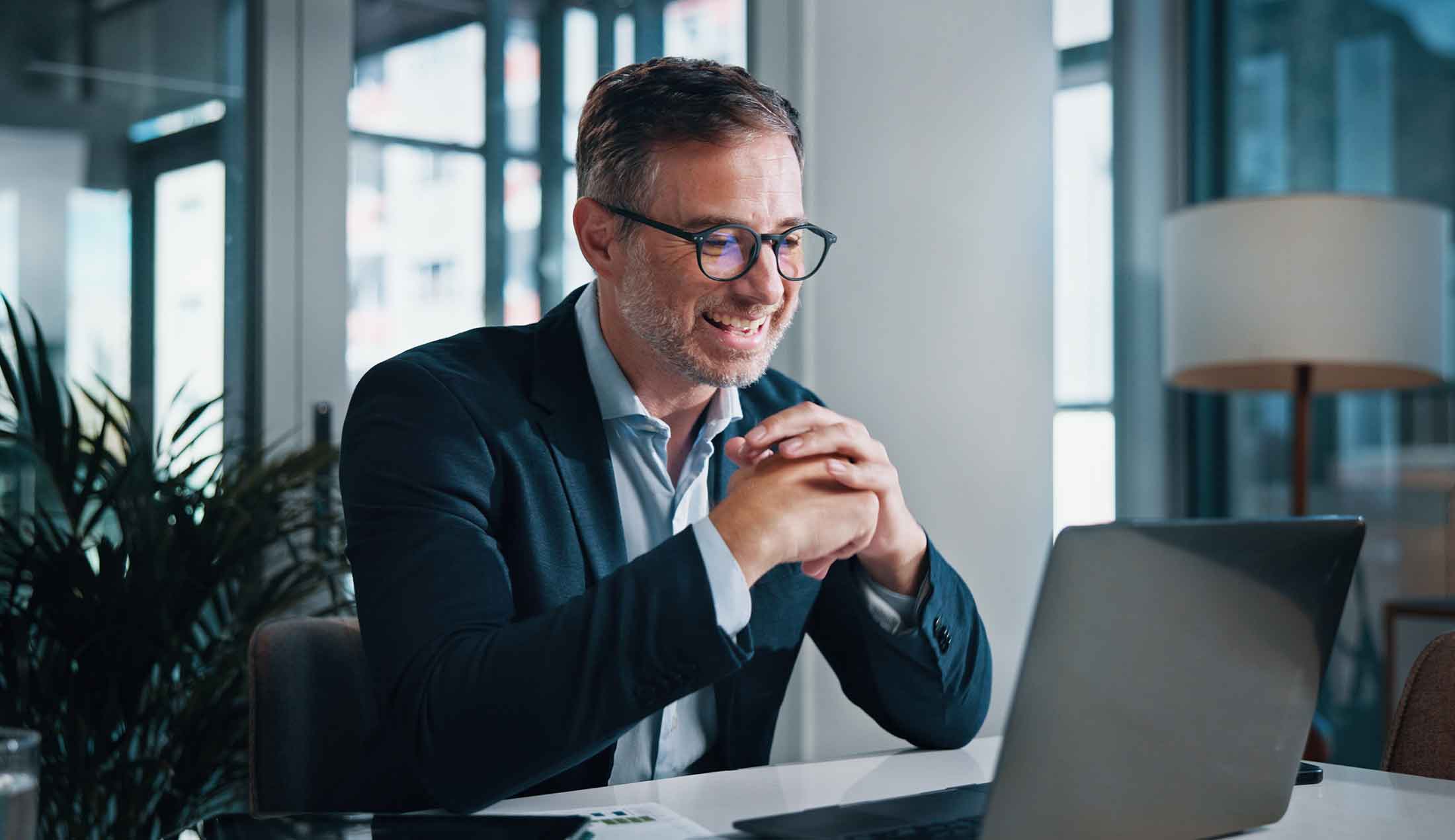 En leende man sitter vid ett skrivbord i kontorsmiljö och tittar på sin skärm